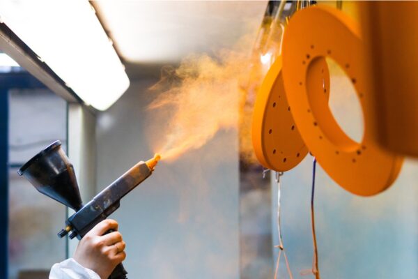 Powder coating of metal parts. A man in a protective suit sprays powder paint from a gun on metal products.